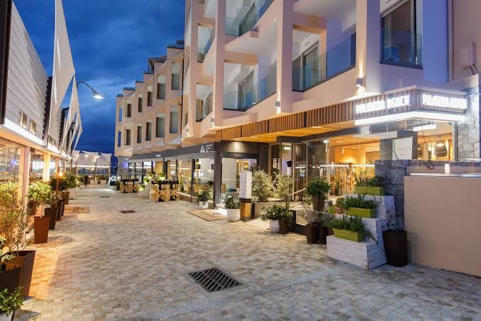 Palmera Beach Hotel & Spa ieeja un vestibila ārpuse vakarā — moderna arhitektūra ar dekoratīviem augiem un apgaismotu ietvi