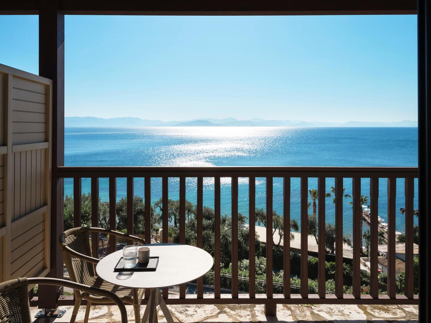 Aeolos Beach Resort numura balkons ar koka margām, galdiņu un krēsliem, no kura paveras skats uz Jonijas jūru Korfu salā.