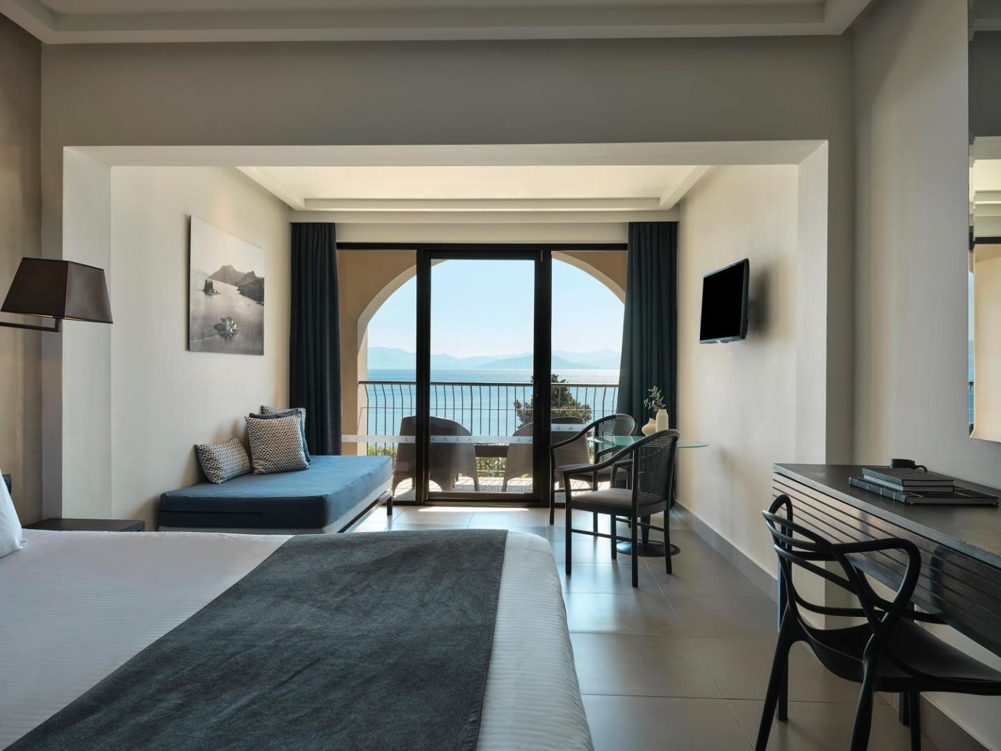 Gaišs Aeolos Beach Resort viesnīcas numurs ar modernu dizainu, atpūtas zonu un balkonu, no kura redzama jūra Grieķijā.