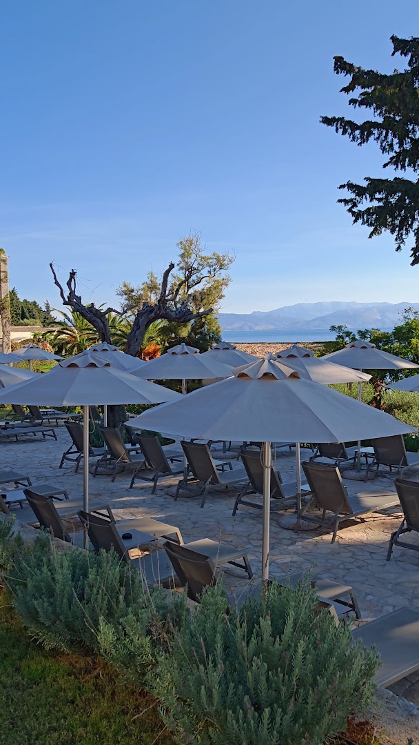 Aeolos Beach Resort atpūtas zona ar sauļošanās krēsliem un saulessargiem uz akmens terases, fonā skats uz Jonijas jūru un kalniem