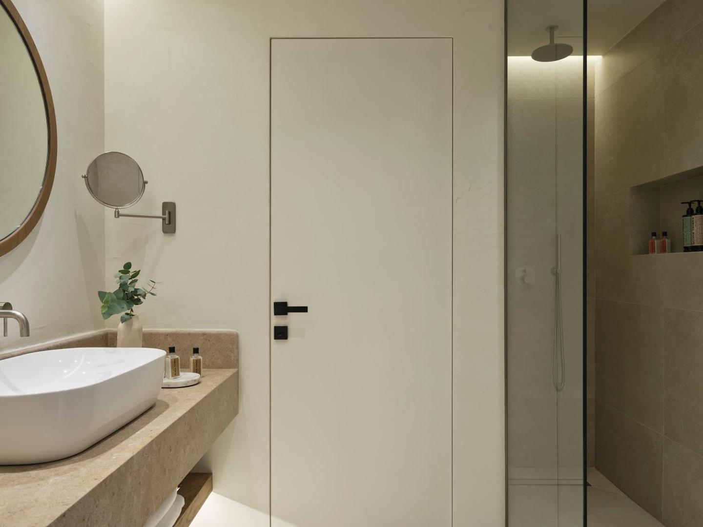 Aeolos Beach Resort numura vannasistaba ar modernu dizainu, baltu izlietni, apaļu spoguli un dušas zonu