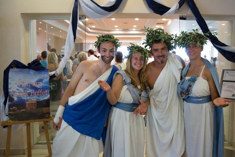 Mareblue Beach Resort personāls grieķu tērpos aicina uz tematisko bufeti Korfu salā — jautra atmosfēra un tradicionāls viesmīlības noformējums