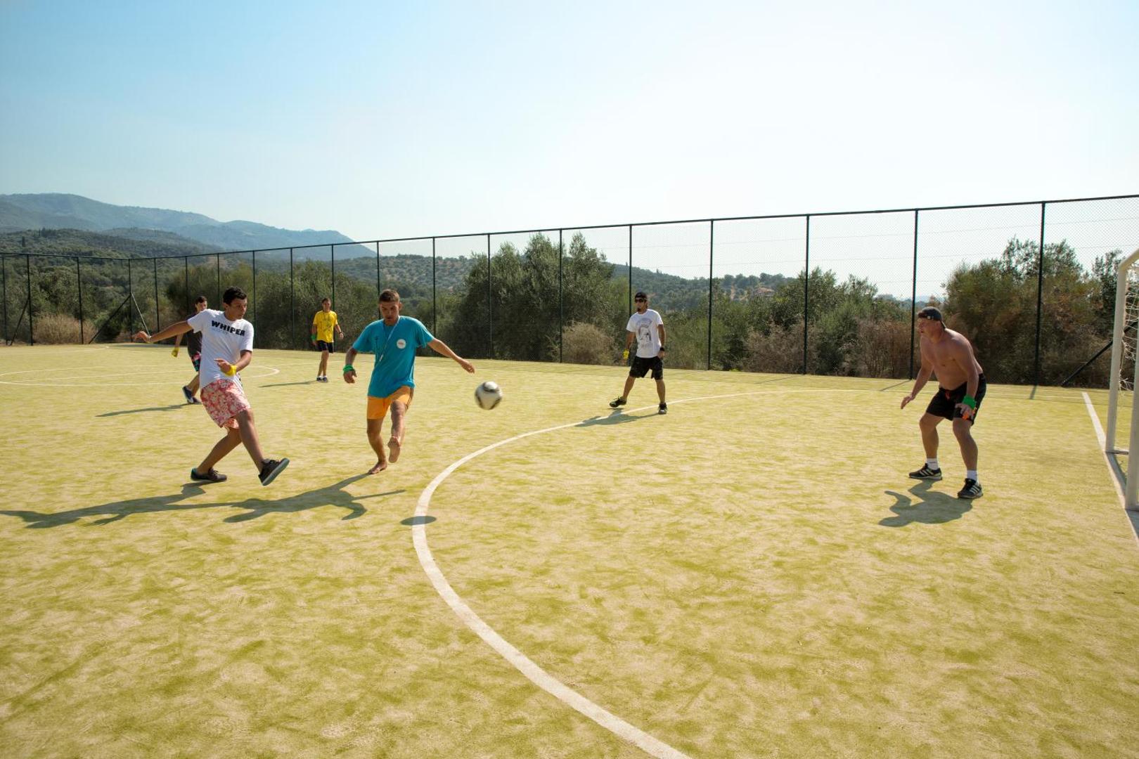 Viesi spēlē futbolu Mareblue Beach Resort sporta laukumā Korfu piekrastē — saulains laiks un aktīvās atpūtas iespējas kūrorta teritorijā