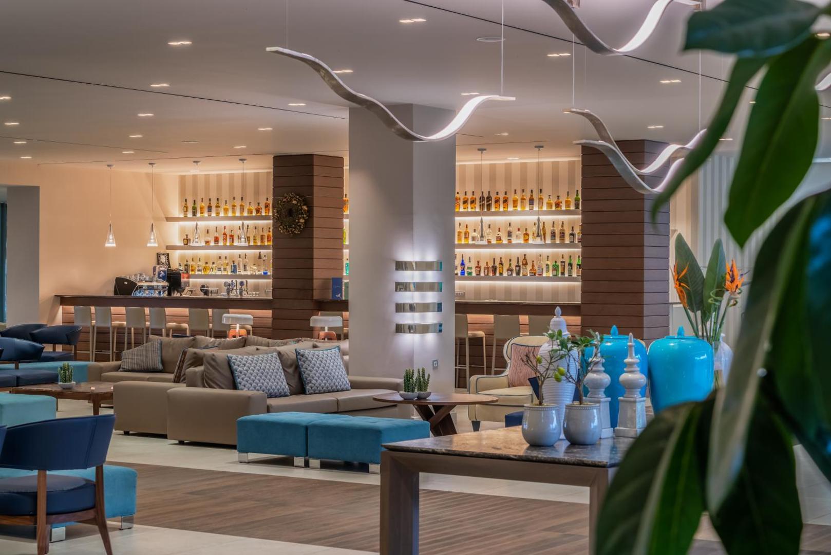 Mareblue Beach Resort modernais lobby bārs un atpūtas zona Korfu salā ar mīkstajiem dīvāniem, stilīgiem gaismas ķermeņiem un plašu dzērienu izvēli