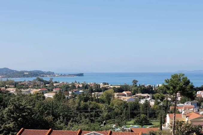Century Resort panorāmas skats uz Aharavi ciematu un Jonijas jūru Korfu salā — zaļojoša apkārtne un piekrastes līnija