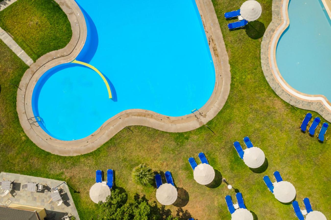 Century Resort Hotel baseina skats no augšas, izceļot zilo ūdeni, zaļo zālienu un baltos saulessargus Korfu kūrortā.