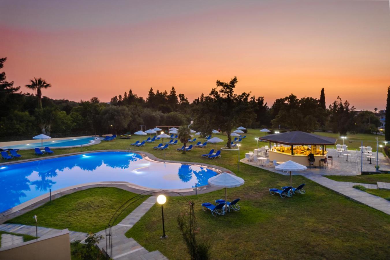 Century Resort Hotel baseina bārs un atpūtas zona vakara gaismās ar izgaismotu baseinu un krēslas debesīm.