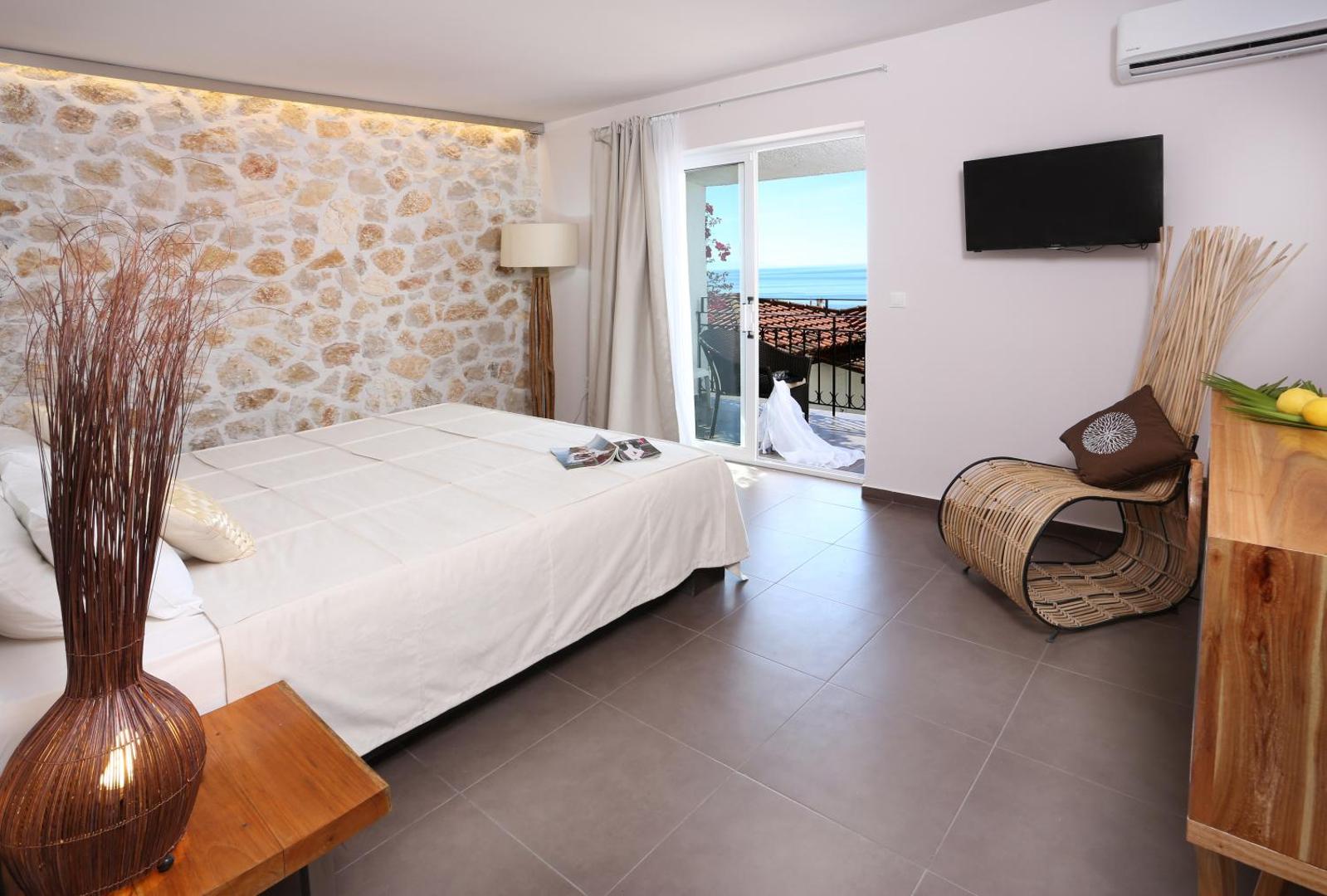 Pantokrator Hotel gaišs numurs ar dekoratīvu akmens sienu, balkonu un skatu uz jūru — moderns interjers ar pītu atpūtas krēslu