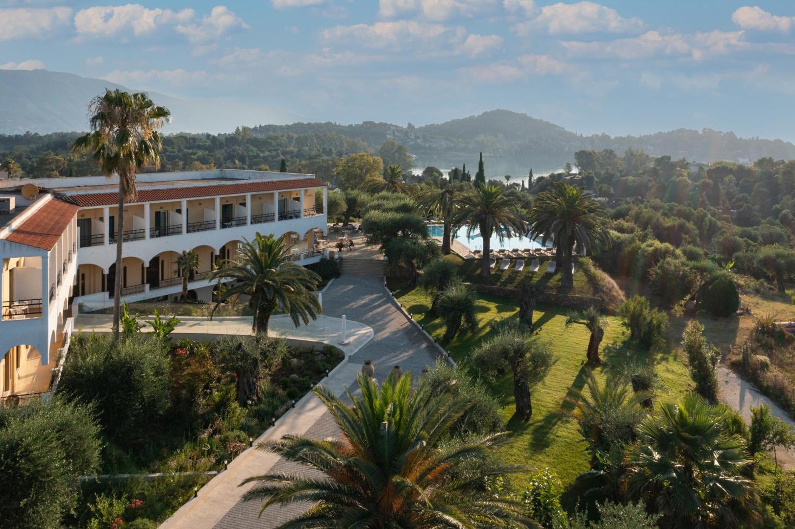 Paradise Corfu viesnīcas ēka un dārzs ar palmām Korfu salā — skats uz apkārtnes kalniem un jūras līci tālumā