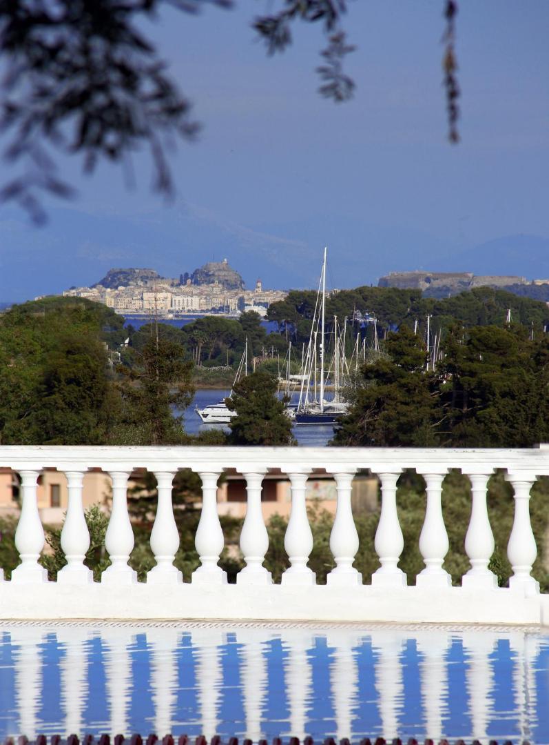 Skats no Paradise Corfu terases ar baltu margu uz jahtām un vēsturisko Korfu pilsētas cietoksni tālumā