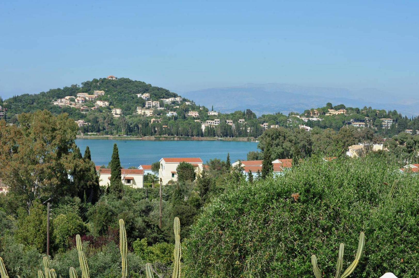 Skats no Paradise Corfu uz zaļajiem pakalniem, ciemata mājām un zilo jūras līci Korfu salā