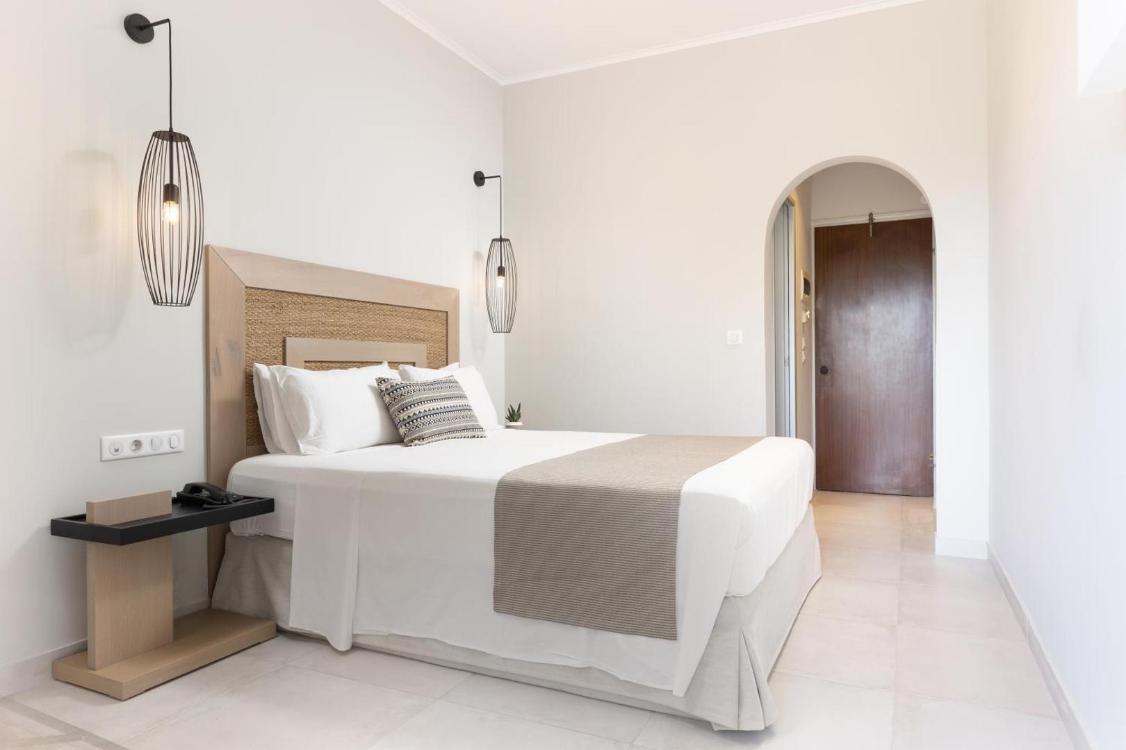 Paradise Corfu viesnīcas elegants numurs ar oša koka detaļām, dizaina lampām un arkas eju uz priekštelpu.