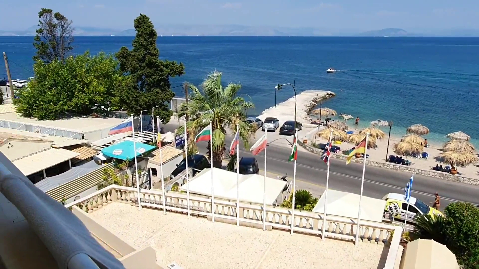 Skats no Potamaki Beach viesnīcas terases uz Jonijas jūru, pludmali ar saulessargiem un piestātni Benitsē