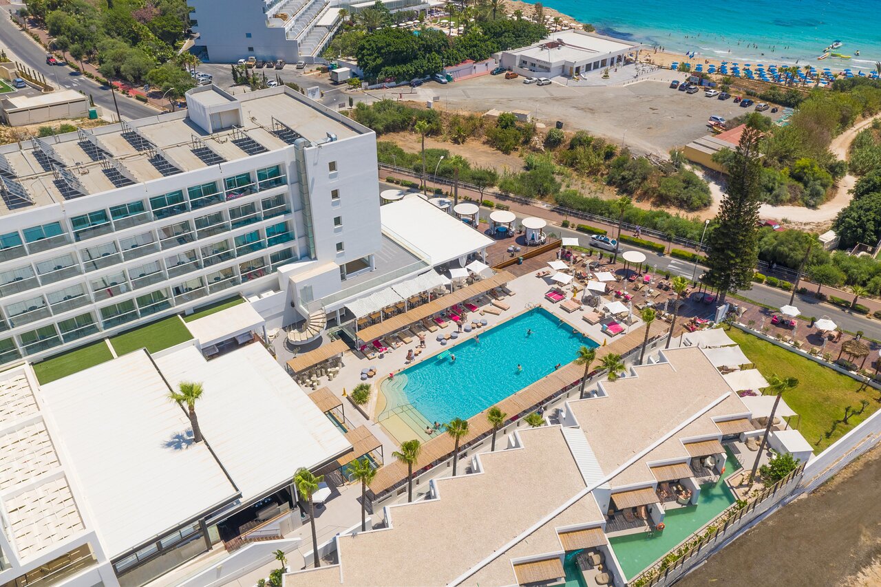 Napa Mermaid Hotel āra baseina zona no augšas — sauļošanās krēsli, bārs un numuri ar tiešu piekļuvi baseinam Ajanapā.