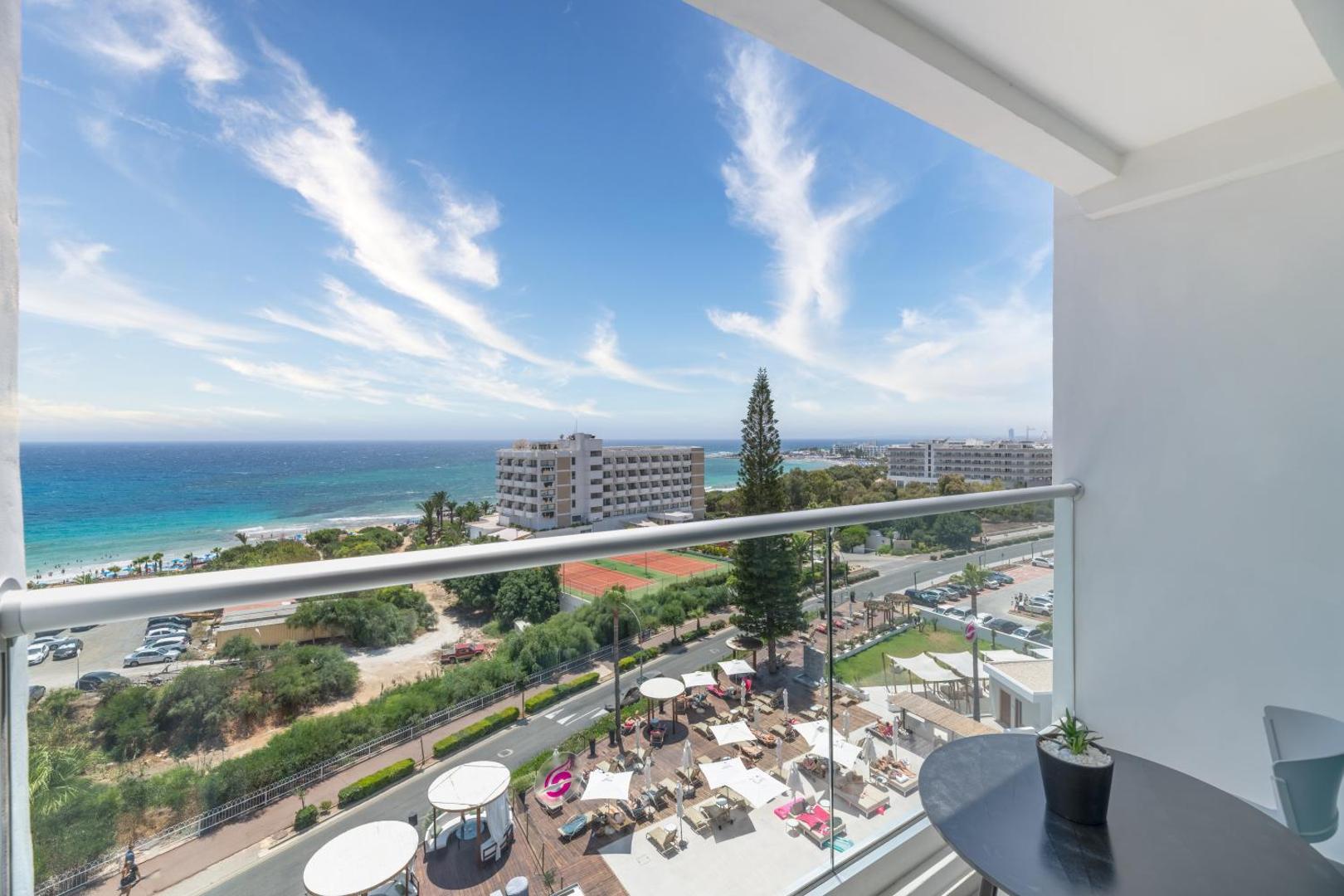 Skats no Napa Mermaid Hotel balkona uz pludmali, tenisa kortiem un kūrorta apkārtni Ajanapā saulainā dienā