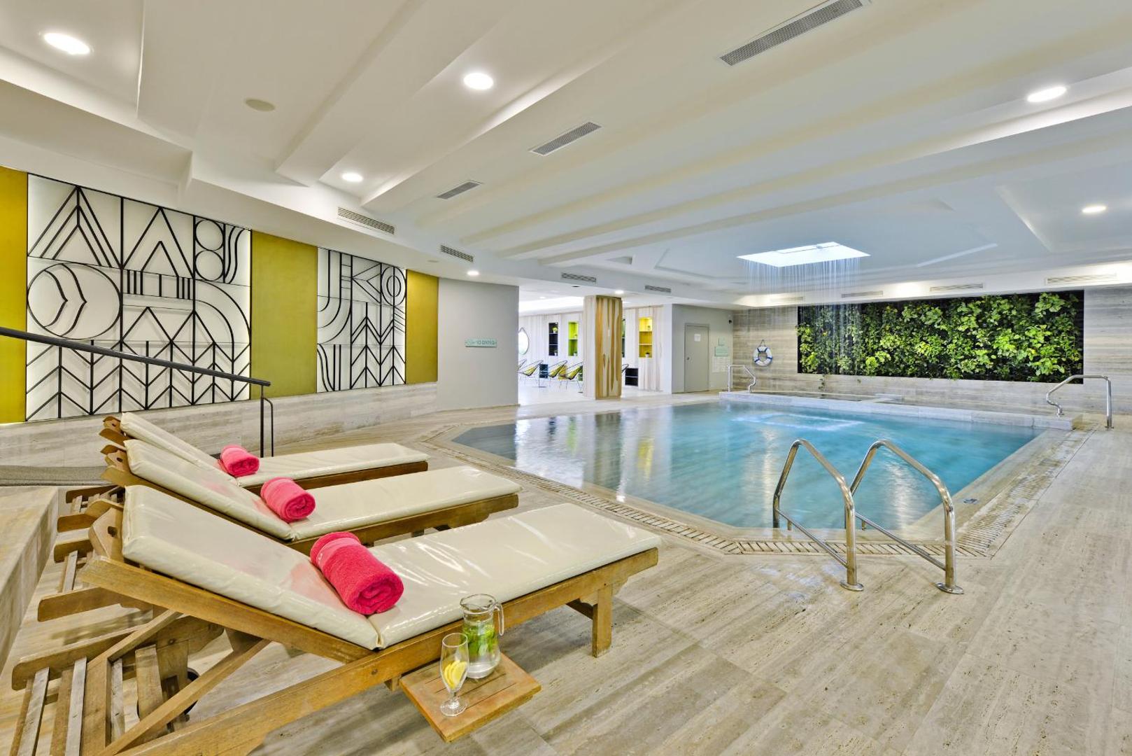 Napa Mermaid Hotel iekštelpu baseins ar koka sauļošanās krēsliem, dekoratīvu sienu un zaļo augu zonu spa centrā Aijanapā