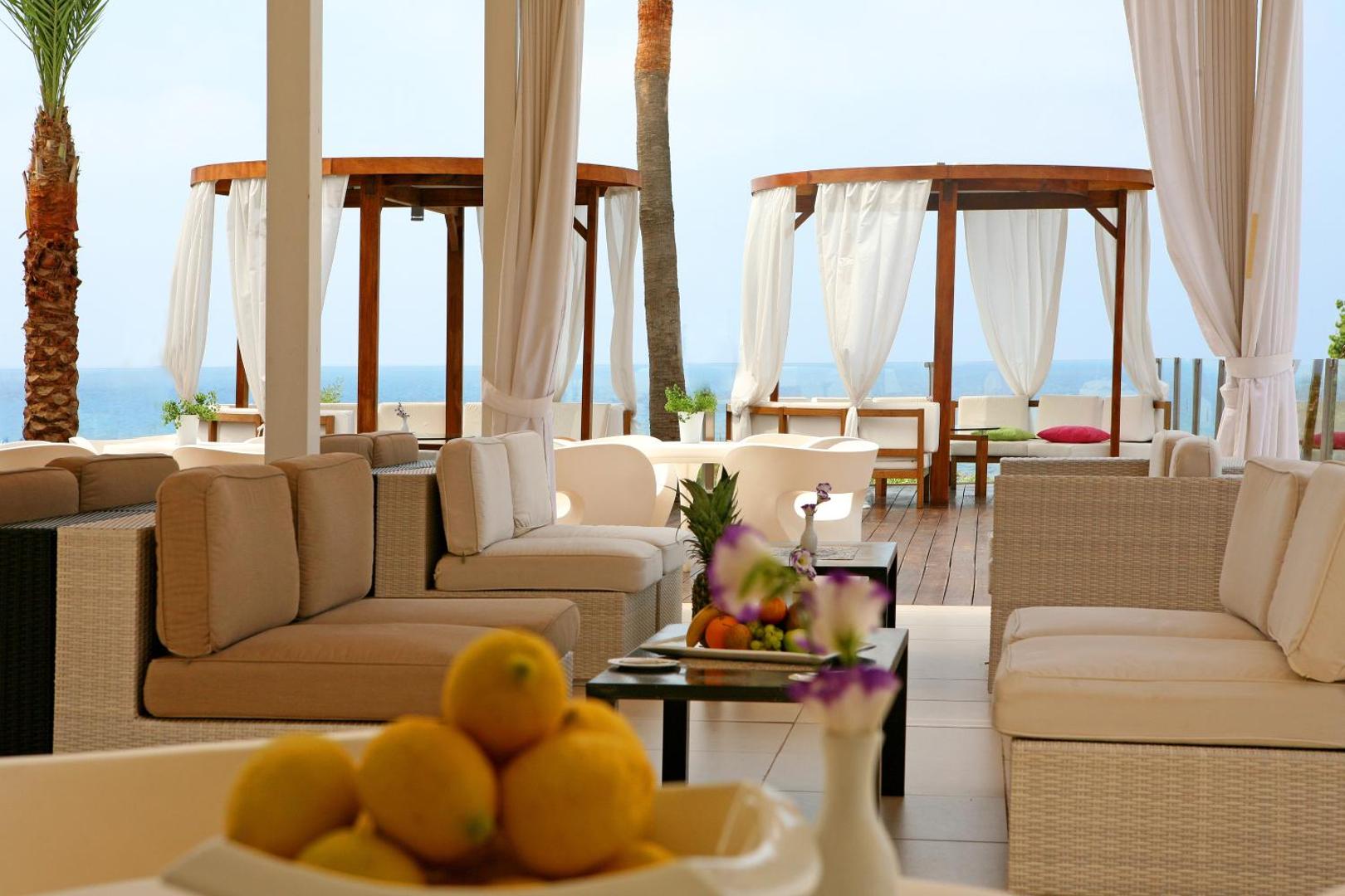 Napa Mermaid Hotel terase ar gaišām mēbelēm un privātām nojumēm piekrastē Aijanapā — skats uz Vidusjūru un dekoratīviem citrusaugļiem