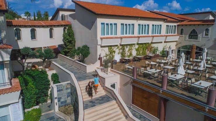 Napa Plaza viesnīcas iekšpagalms ar kāpnēm un āra terasi restorānam — gaiša arhitektūra un Vidusjūras stila apstādījumi