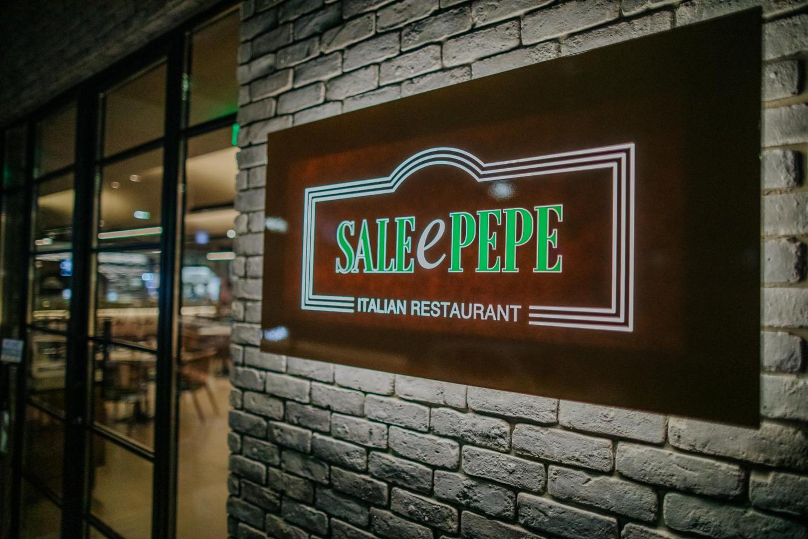 Napa Plaza viesnīcas itāļu restorāna Sale e Pepe izkārtne pie mūra sienas Aijanapā, Kiprā — ieeja modernā ēdināšanas zonā