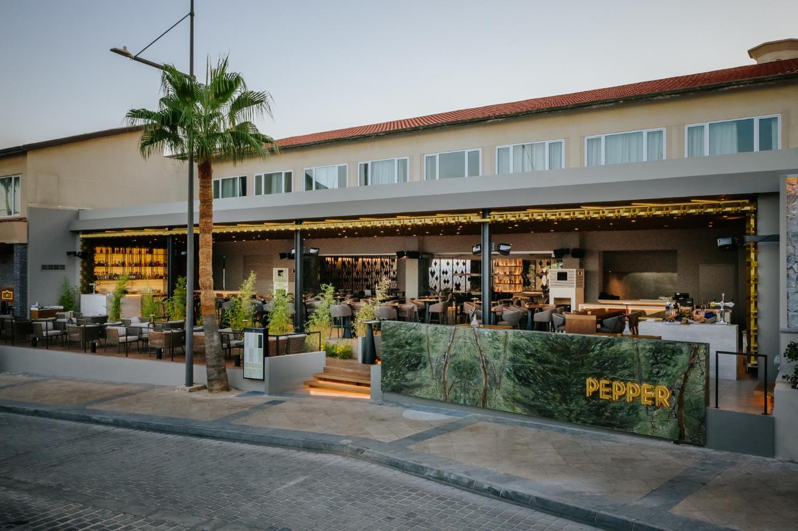 Napa Plaza viesnīcas restorāns Pepper Aijanapā — moderna terase ar palmu, zaļām marmora detaļām un vakara apgaismojumu pie ielas