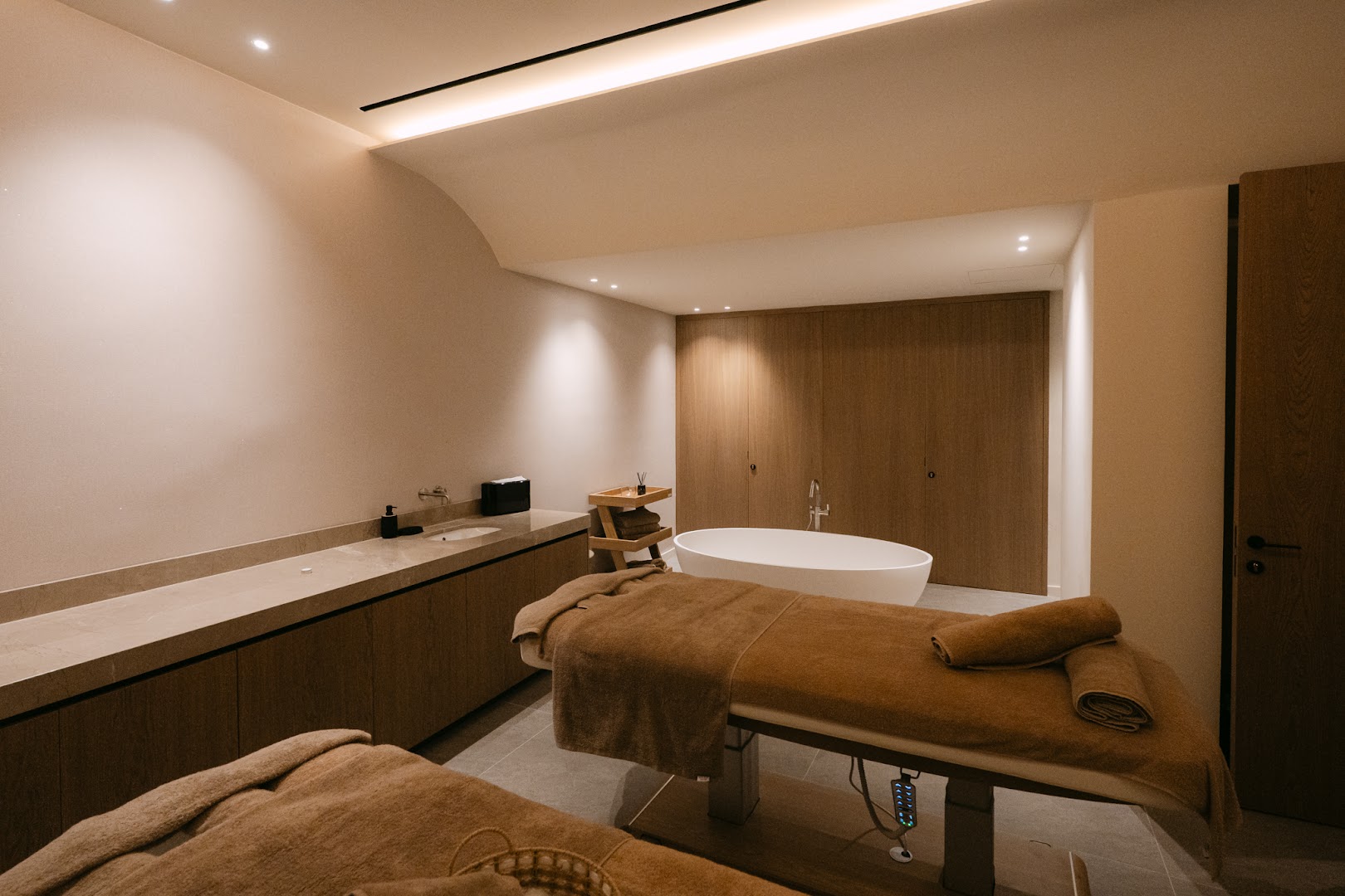 Napa Plaza spa procedūru telpa ar masāžas galdiem un brīvstāvošu vannu gaišos, siltos toņos