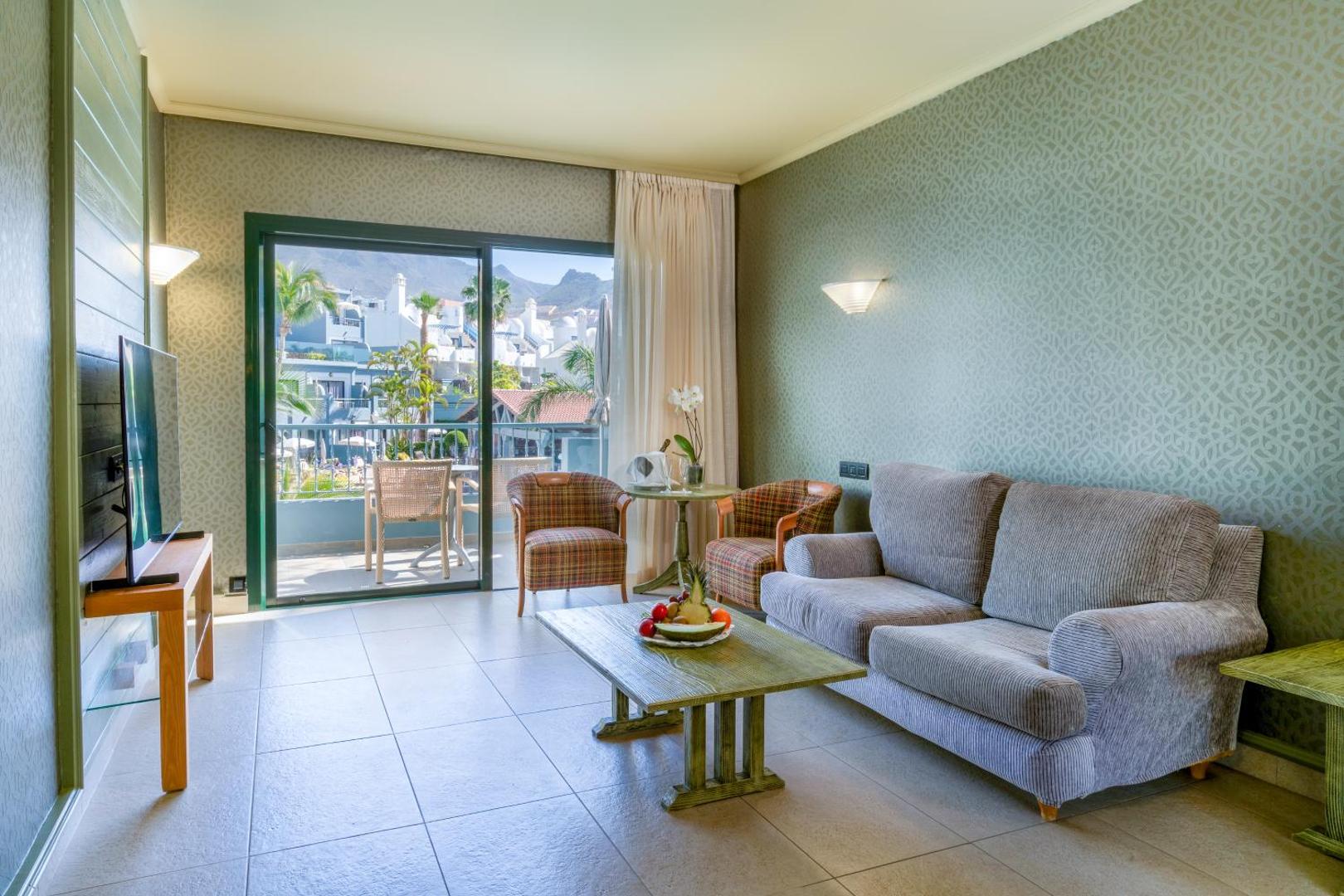 Hotel Colon Guanahani viesistabas zona ar pelēku dīvānu, atpūtas krēsliem un skatu uz balkonu un apkārtnes kalniem.