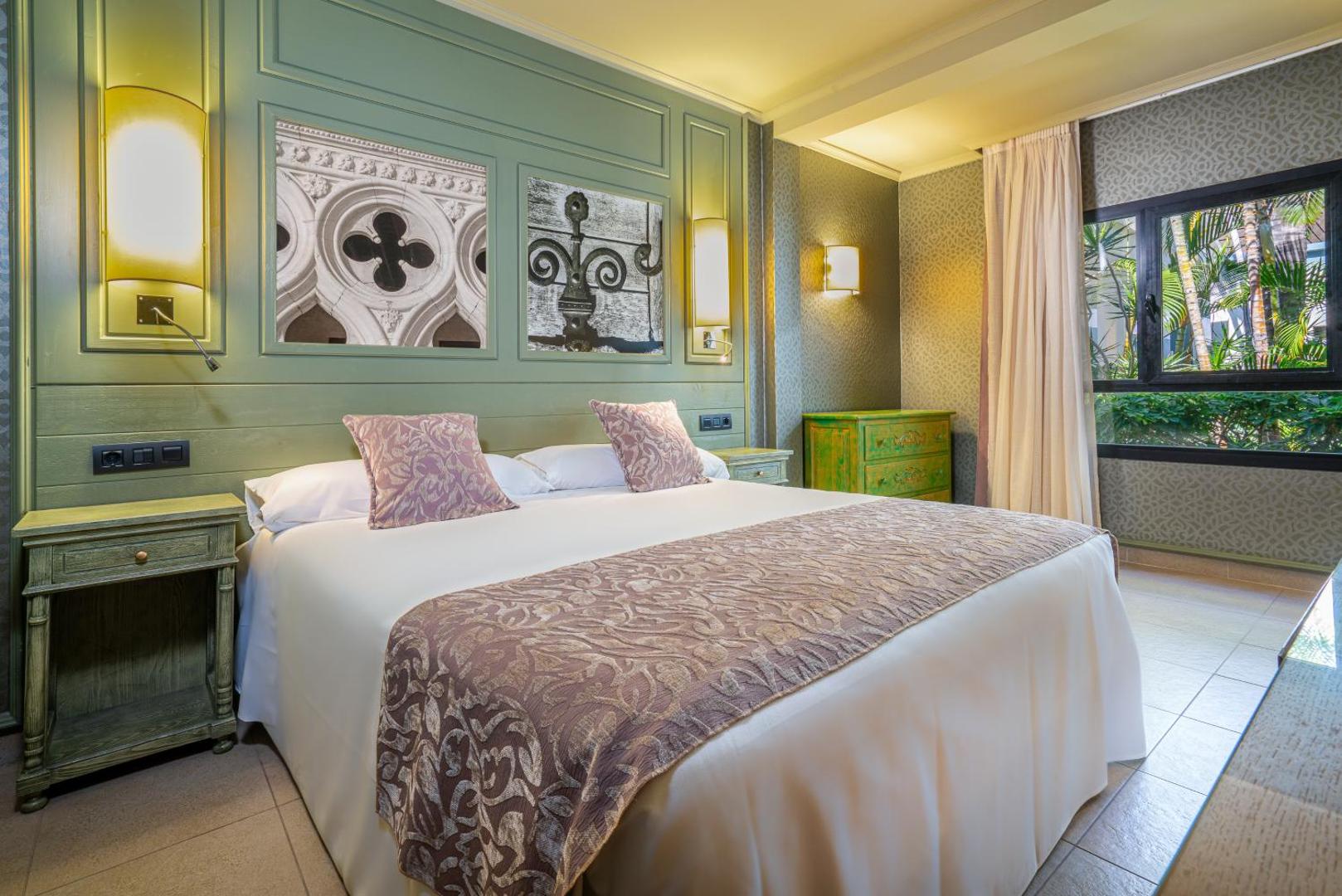 Hotel Colon Guanahani elegants divvietīgs numurs ar zaļganu sienu apdari, koka mēbelēm un lielu gultu Tenerifē, Kanāriju salās.