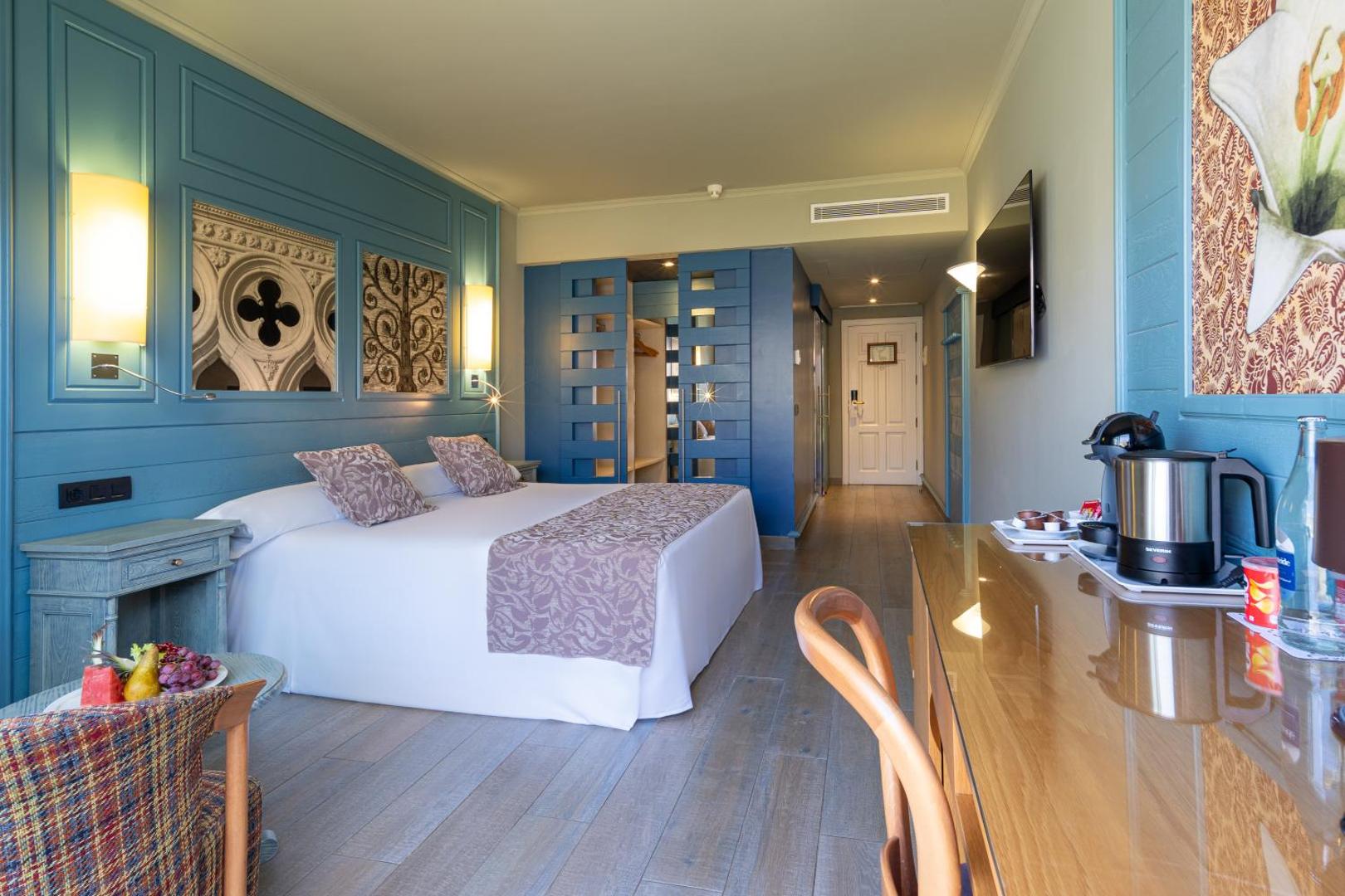 Hotel Colon Guanahani moderns viesnīcas numurs ar zilu sienu paneli, lielu gultu, koka mēbelēm un kafijas pagatavošanas komplektu