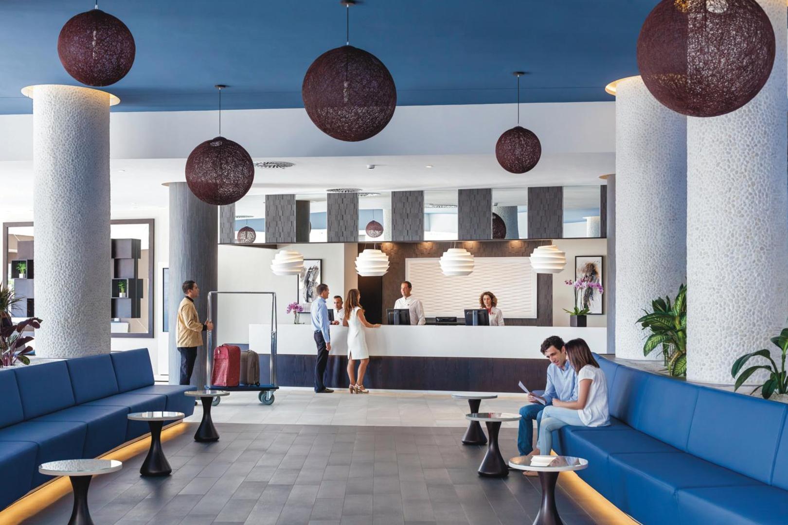 Riu Arecas Hotel lobby zona un recepcija — moderns vestibils ar ziliem dīvāniem, augstiem griestiem un stilīgiem gaismekļiem