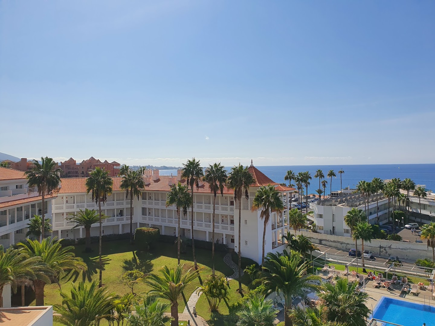 Riu Arecas Hotel teritorijas skats no augšas ar baltām ēkām, palmu dārzu un zilu baseinu pie okeāna krasta
