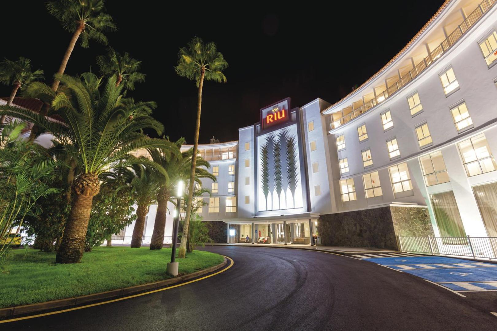 Riu Arecas Hotel galvenā ieeja nakts apgaismojumā Tenerifē — moderna fasāde ar palmām un izgaismotu viesnīcas logo pie piebraucamā ceļa