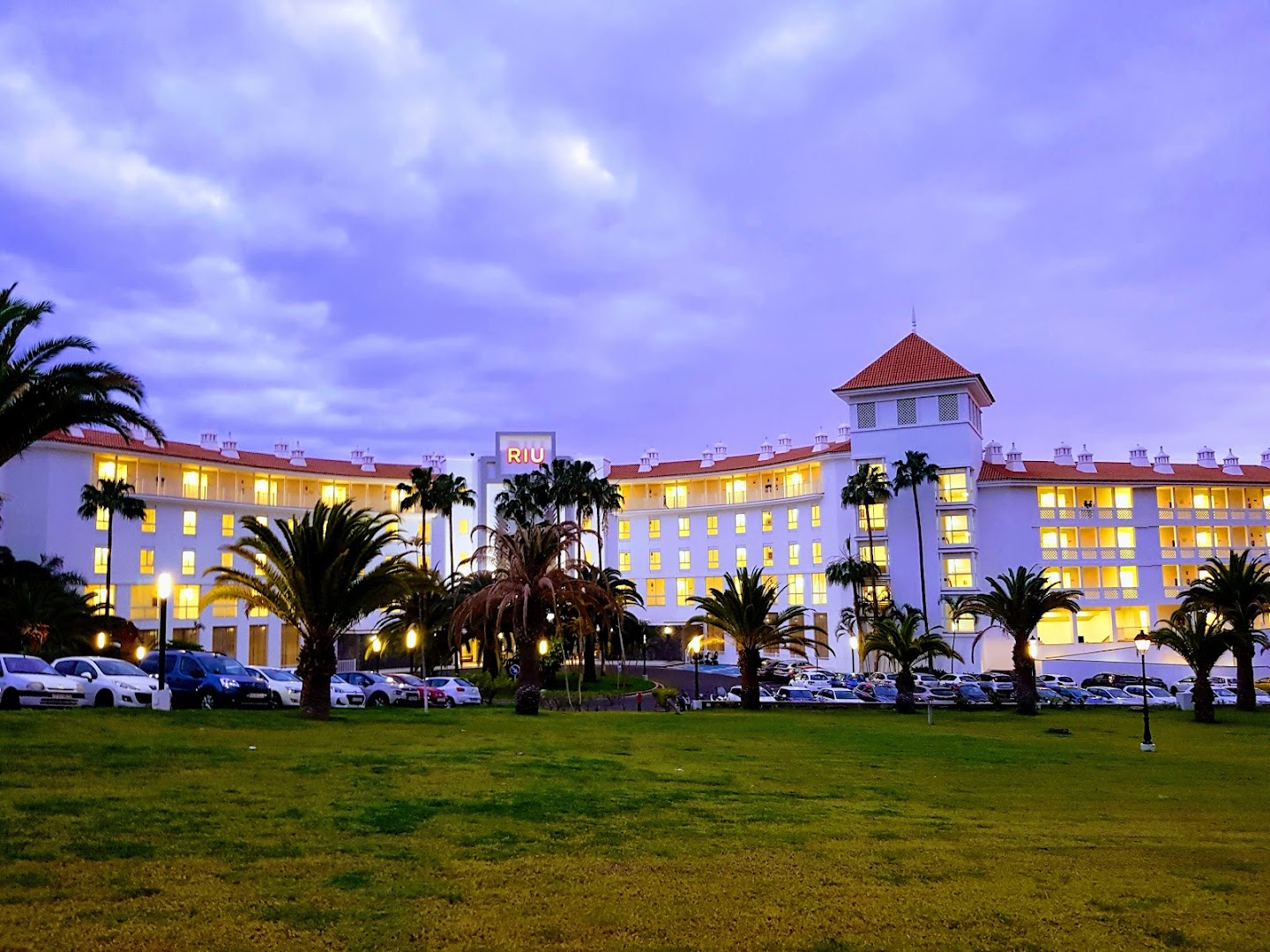Riu Arecas Hotel ēkas kopskats krēslas stundā Tenerifē — izgaismoti numuri, palmas un plašs zālājs viesnīcas priekšplānā