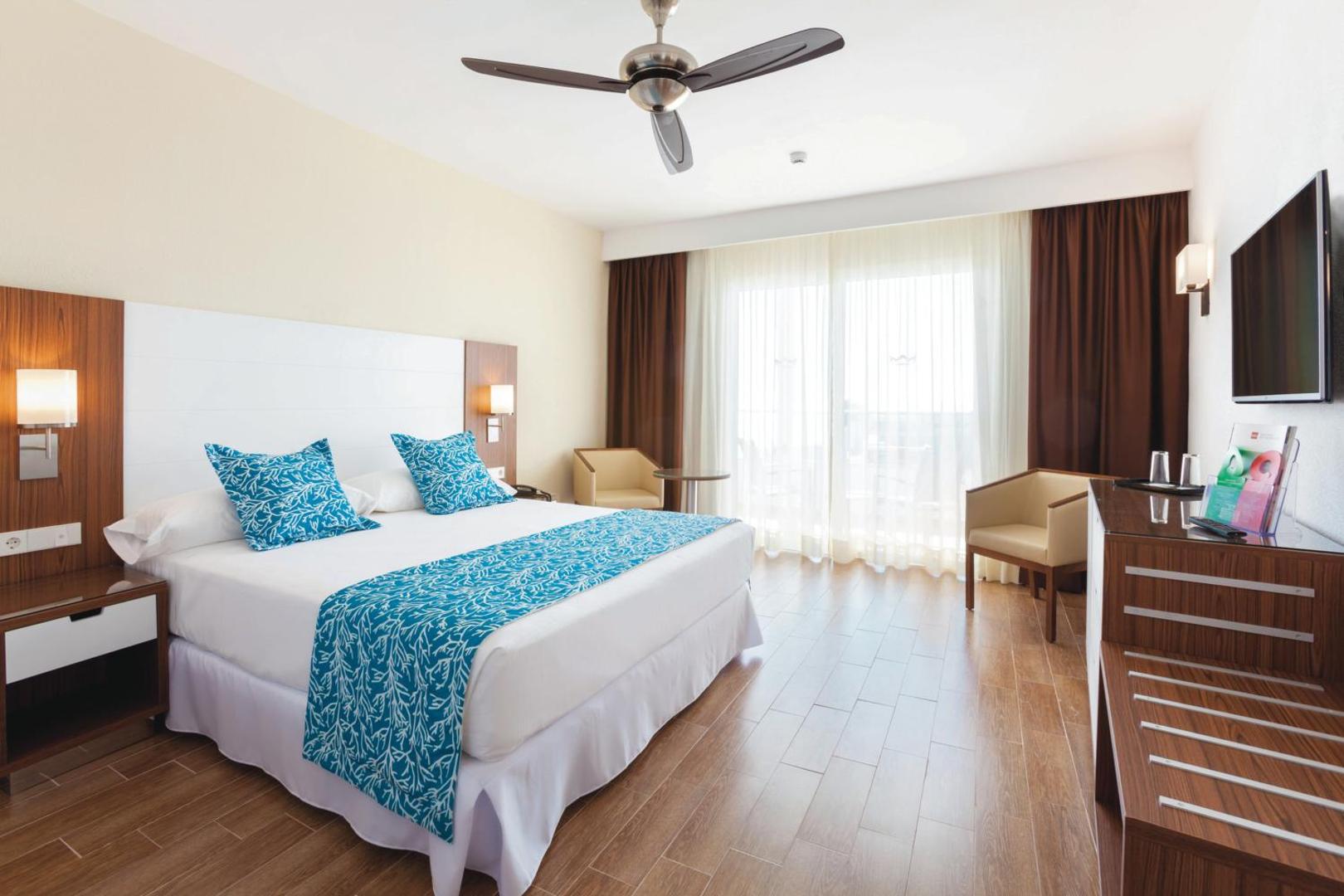 Riu Arecas Hotel gaišs divvietīgs numurs Tenerifē ar koka grīdu, griestu ventilatoru un izeju uz balkonu saulainā dienā
