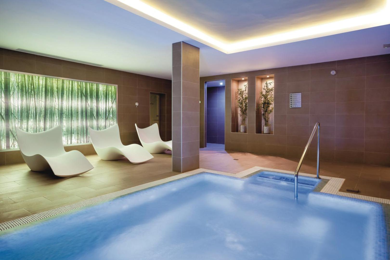 Riu Arecas Hotel spa zonas baseins ar zilu ūdeni, moderniem krēsliem un bambusa dekorācijām pie sienām Tenerifē