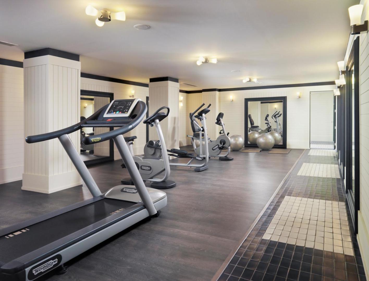 Mūsdienīga H10 Big Sur viesnīcas fitnesa zāle ar Technogym skrejceliņiem, velotrenažieriem un vingrošanas bumbām gaišā interjerā