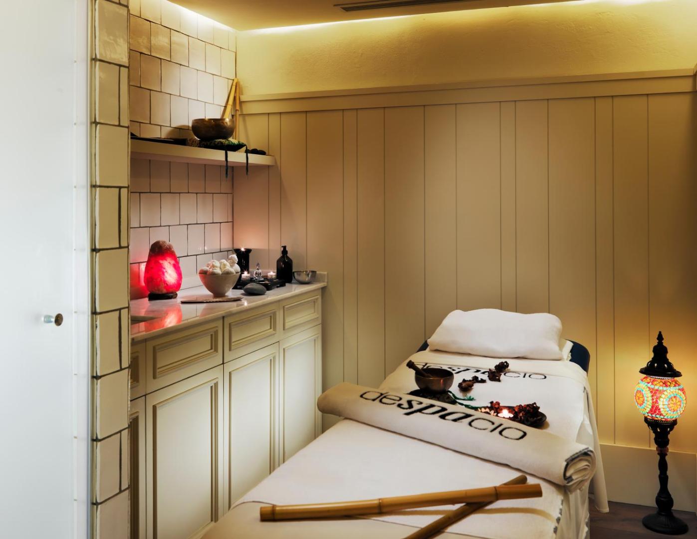 H10 Big Sur viesnīcas Despacio spa masāžas telpa ar relaksējošu apgaismojumu, masāžas galdu un austrumu stila dekorācijām