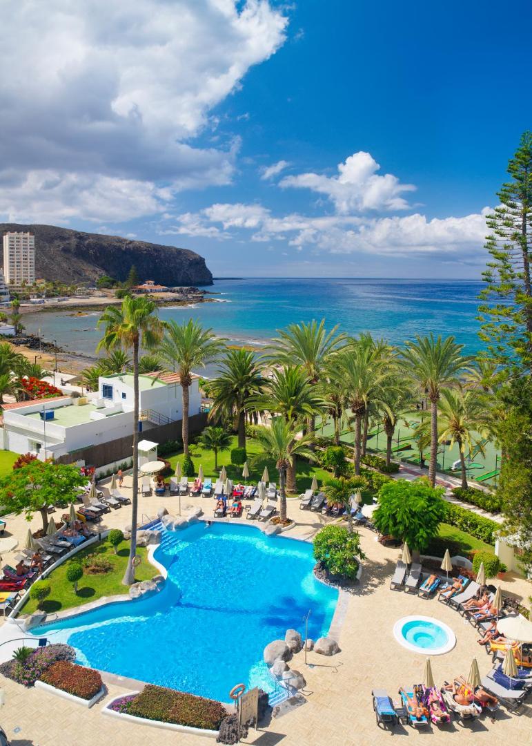 Skats no augšas uz H10 Big Sur baseinu, dārzu un okeāna piekrasti ar kalniem fonā Tenerifē