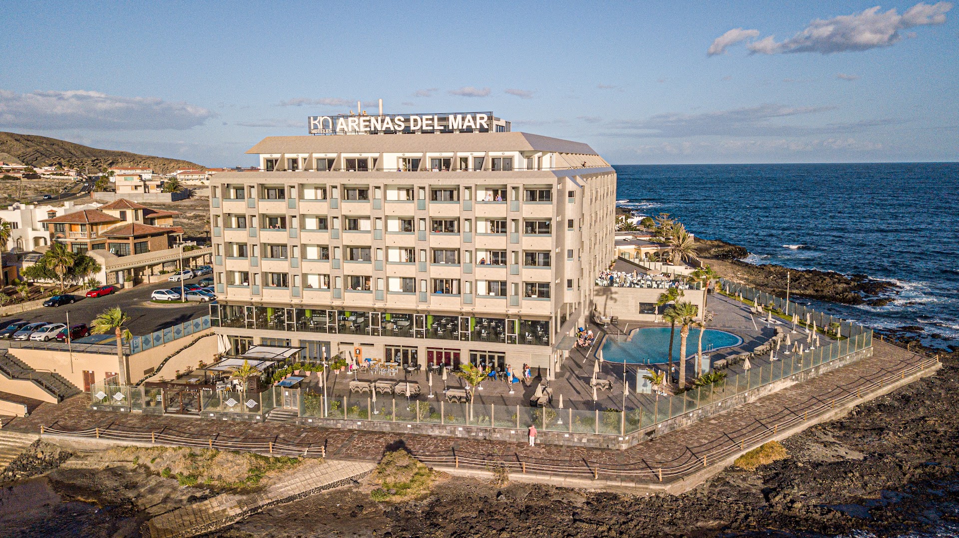 KN Arenas del Mar viesnīcas ēka Tenerifē no putna lidojuma — skats uz baseinu, terasi un okeāna piekrasti saulrietā