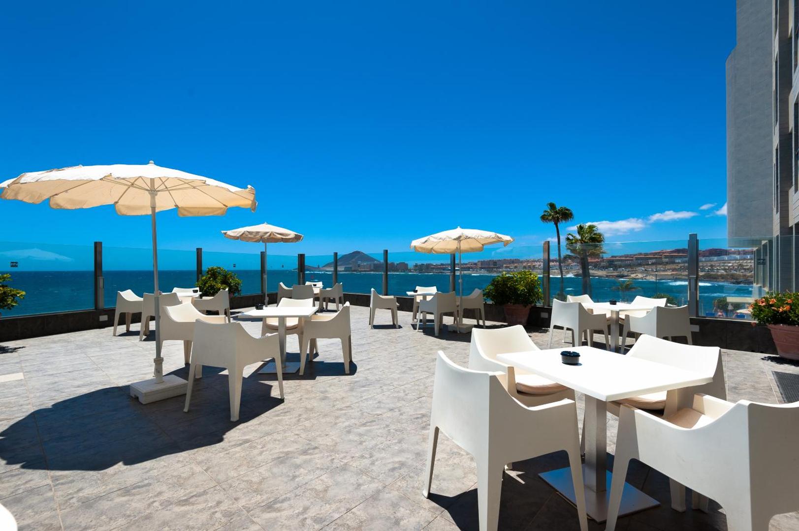 KN Arenas del Mar plašā saulainā terase ar baltām mēbelēm un skatu uz Atlantijas okeānu — moderna atpūtas vieta Tenerifē