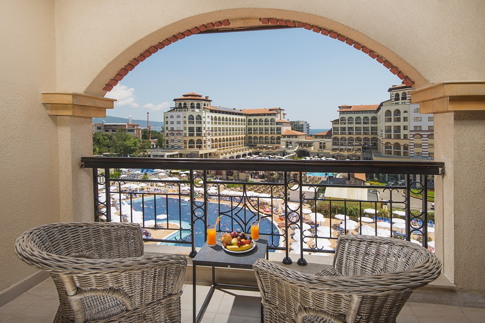 Skats no Melia Sunny Beach Resort balkona uz viesnīcas teritoriju, baseiniem un arhitektūru — atpūtas zona ar pītiem krēsliem