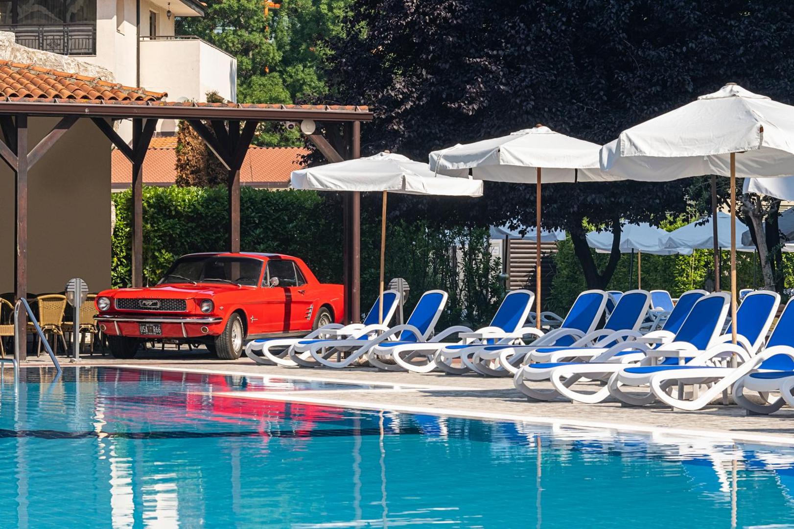 Melia Sunny Beach Resort baseina mala ar sauļošanās krēsliem un dekoratīvu sarkanu retro automašīnu pie bāra zonas