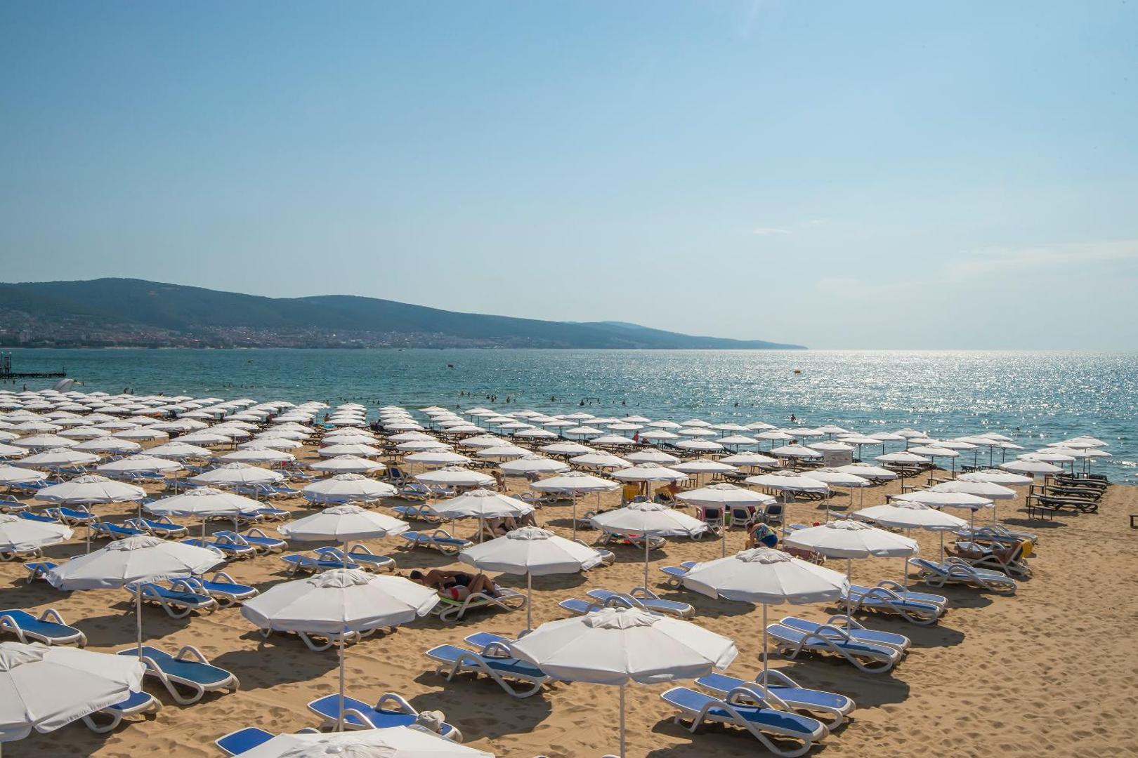 Melia Sunny Beach Resort privātā pludmale Bulgārijā ar baltiem saulessargiem un ziliem sauļošanās krēsliem pie Melnās jūras krasta līnijas