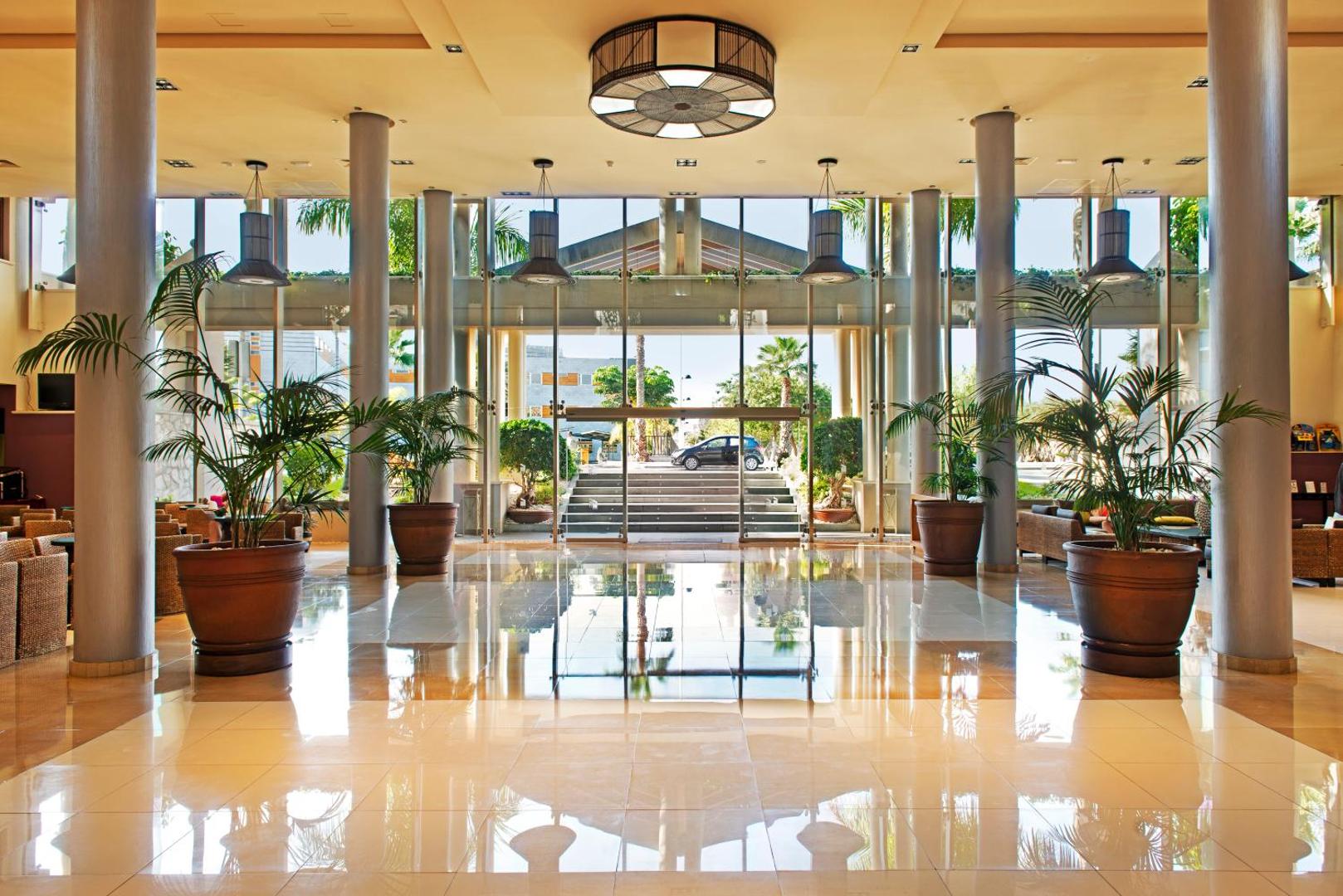 Marylanza Suites & Spa gaišais un plašais vestibils Tenerifē ar lieliem logiem, palmām podos un pulētu flīžu grīdu, kas atspoguļo gaismu.