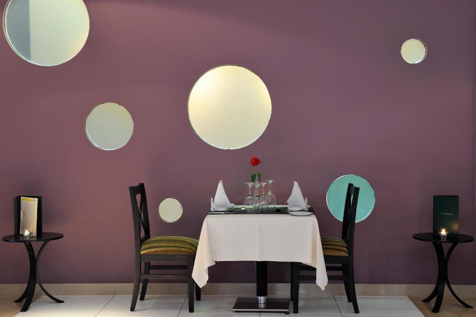 Marylanza Suites & Spa romantisks galdiņš diviem pie violetas sienas ar apaļiem spoguļiem un dekoratīvu rozi