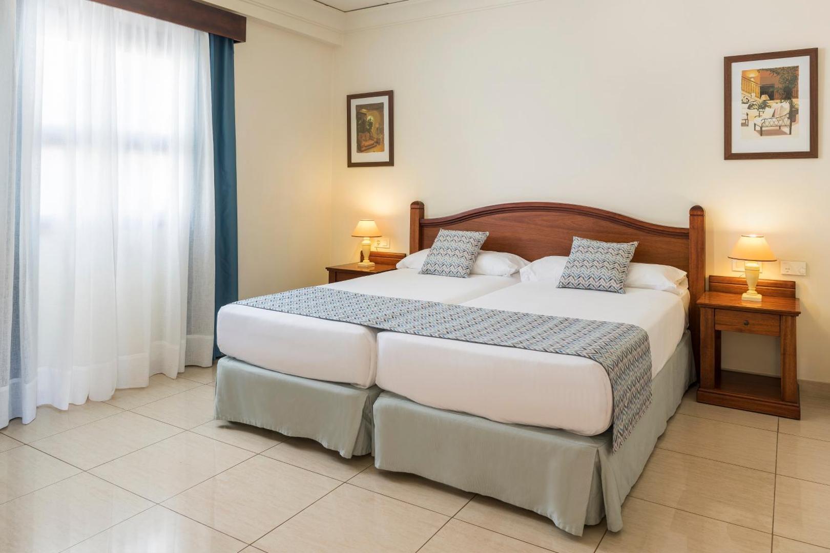 Marylanza Suites & Spa gaišs guļamistabas numurs ar divām gultām, koka mēbelēm un klasisku interjeru siltos toņos
