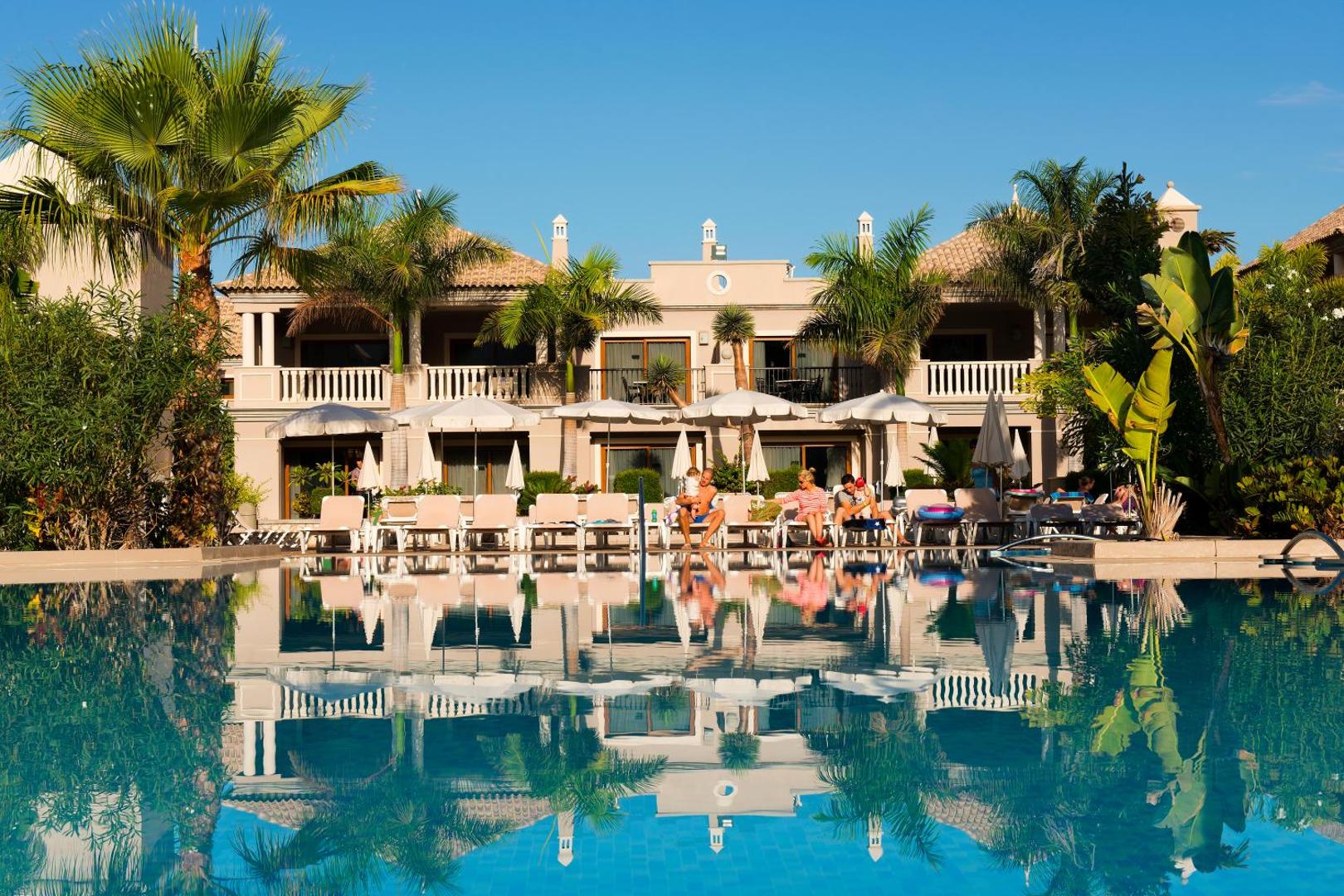 Marylanza Suites & Spa galvenais āra baseins ar saulessargiem un atpūtas krēsliem pie viesnīcas ēkas Tenerifē saulainā dienā.