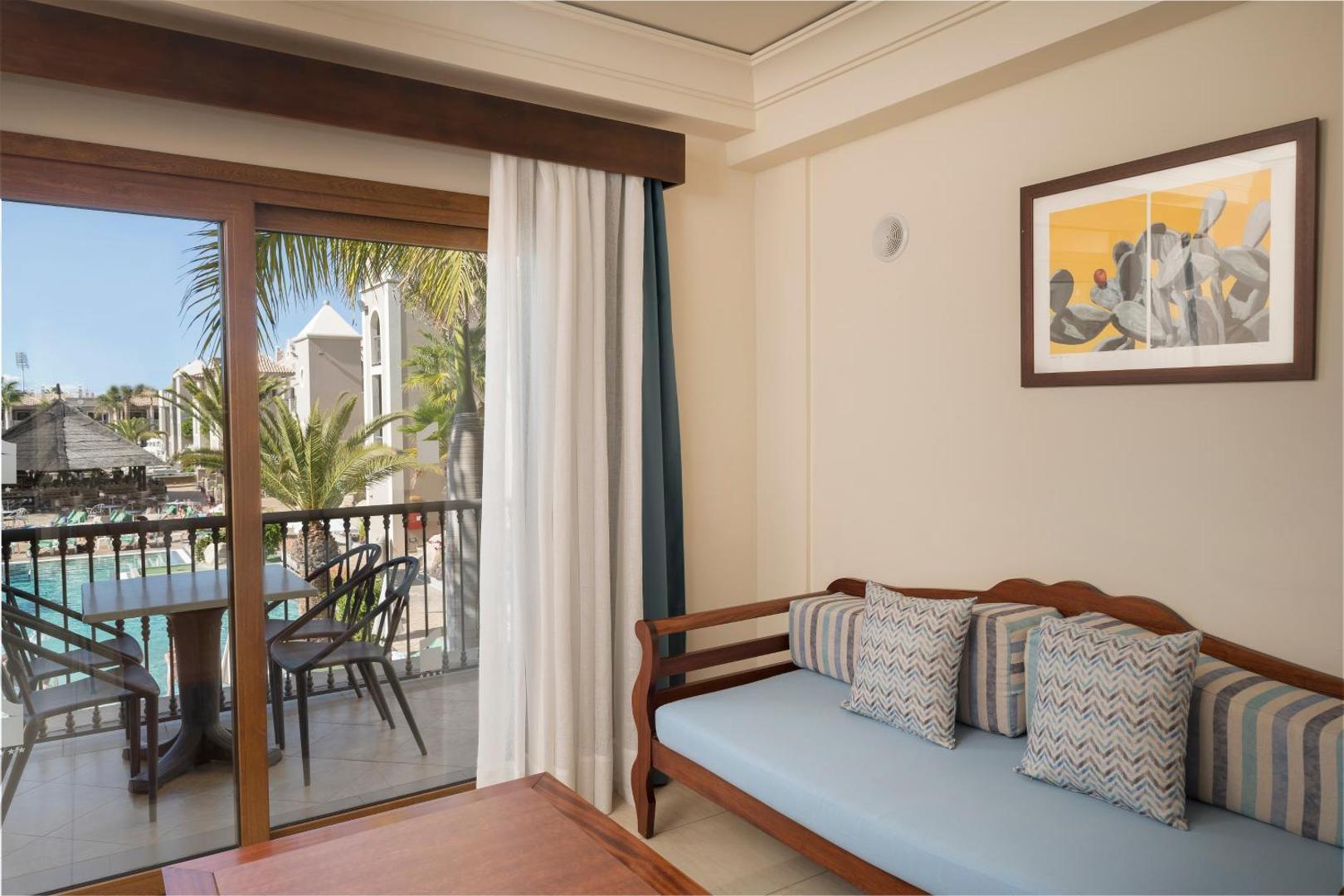 Marylanza Suites & Spa numura atpūtas zona ar gaiši zilu dīvānu un skatu uz balkonu, no kura paveras skats uz baseinu Tenerifē.
