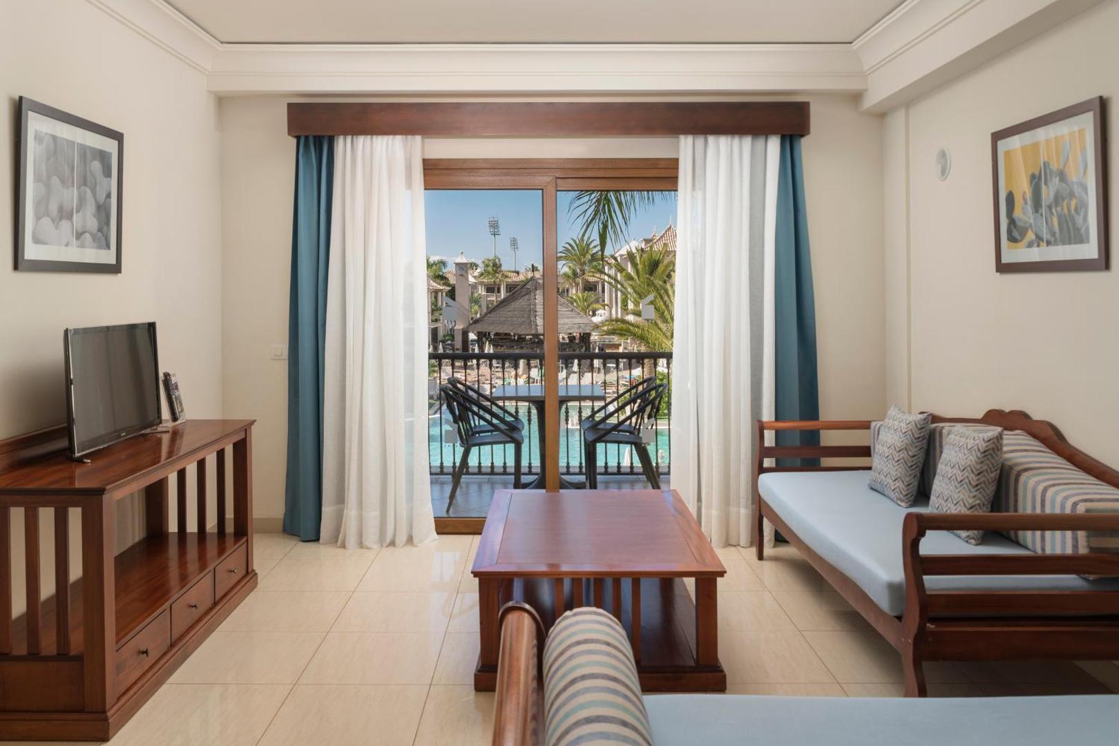 Marylanza Suites & Spa viesnīcas numura interjers ar koka mēbelēm, televizoru un izeju uz balkonu Tenerifes kūrortā.