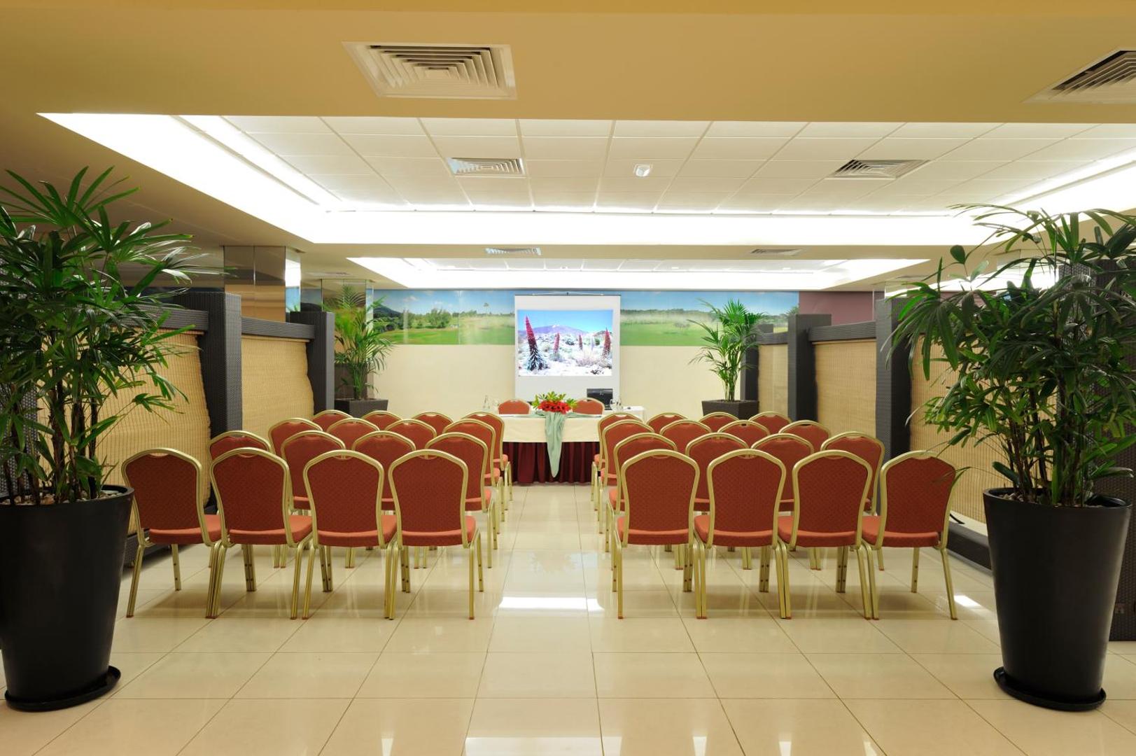 Marylanza Suites & Spa konferenču zāle ar sarkanajiem krēsliem, prezentāciju ekrānu un dekoratīviem augiem podos