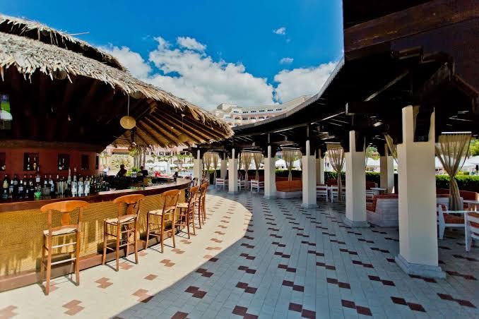 DIT Majestic Beach Resort pludmales bārs ar salmu jumtu, koka krēsliem un plašu āra terasi pie jūras krasta